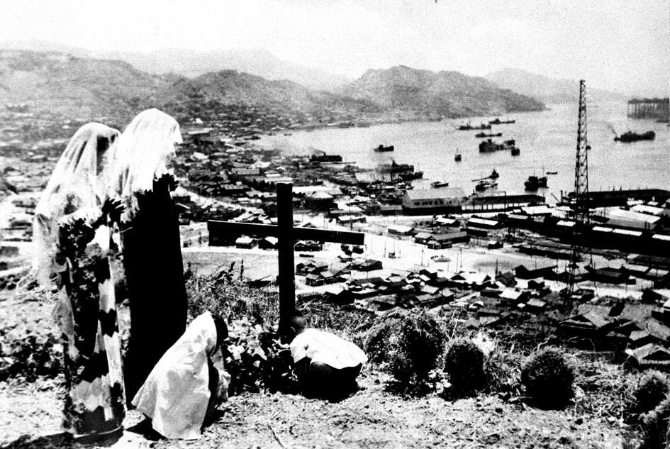 Catholics pray on Aug. 1, 1947, roughly two years after the bombing, as rebuilding work continues at the port of Nagasaki. (Kyodo)