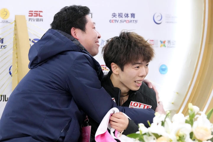 男子フリーの得点を確認し、日下匡力コーチ(左)と抱き合う佐藤駿=重慶(共同)