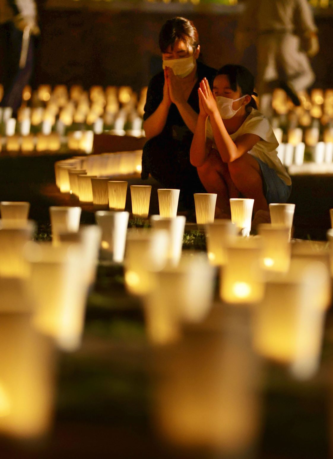 長崎市の爆心地公園に並べられたキャンドルに手を合わせる親子＝2022年8月8日夜